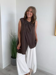 Model wearing asymmetric buttoned sleeveless vest top – relaxed fit and draped silhouette