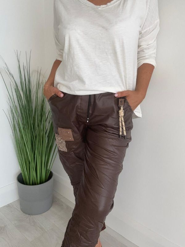 Women’s leatherette joggers in faux leather with soft fleece lining, elastic waistband, adjustable drawstring, side pockets, and patch detail. 