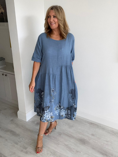 Model wearing a crinkle-textured midi dress with blue floral and butterfly hem detail, scoop neckline, and side pockets — perfect for spring and summer styling