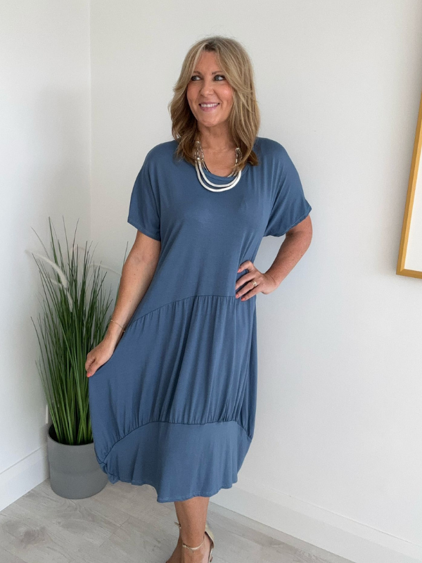 Model wearing a relaxed fit tunic dress with an asymmetric tiered hem, short sleeves, and round neckline, styled for casual comfort and everyday elegance