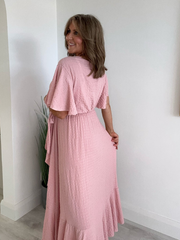 Model wearing an elegant plus size wrap maxi dress with flutter sleeves, tie waist, and asymmetrical hem, designed for UK sizes 14–24, styled for a flattering and flowy summer look.