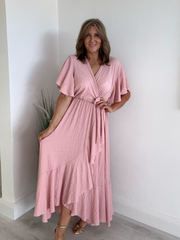 Model wearing an elegant plus size wrap maxi dress with flutter sleeves, tie waist, and asymmetrical hem, designed for UK sizes 14–24, styled for a flattering and flowy summer look
