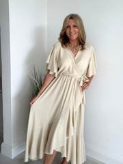 Model wearing an elegant plus size wrap maxi dress with flutter sleeves, tie waist, and asymmetrical hem, designed for UK sizes 14–24, styled for a flattering and flowy summer look