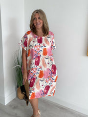 Woman wearing a floral print linen midi dress with multicolored flowers print, standing indoors and smiling.