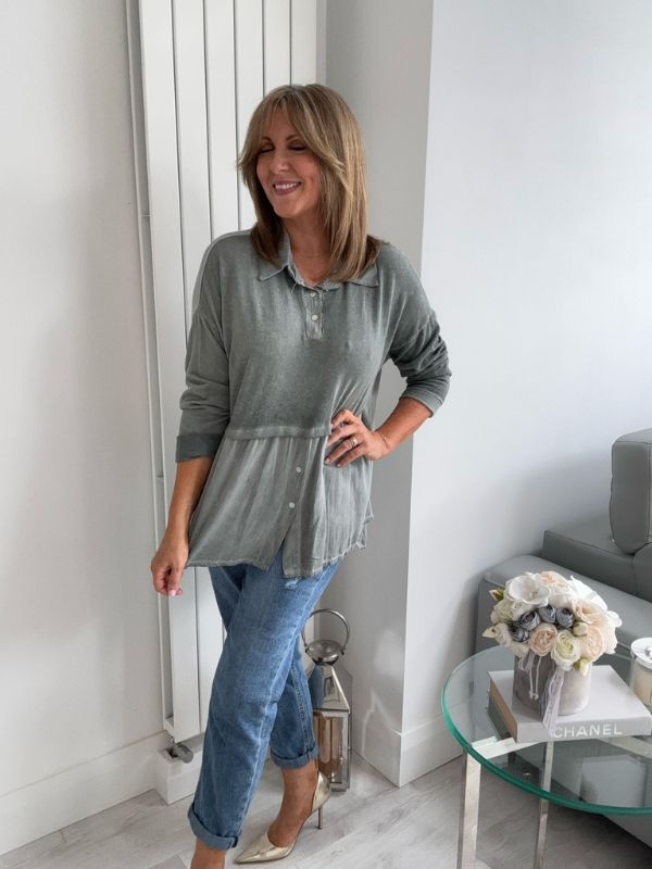 Woman wearing a vintage rose two-tone blouse with button details, paired with blue jeans and gold pointed flats, standing indoors by a round glass table and a flower arrangement.