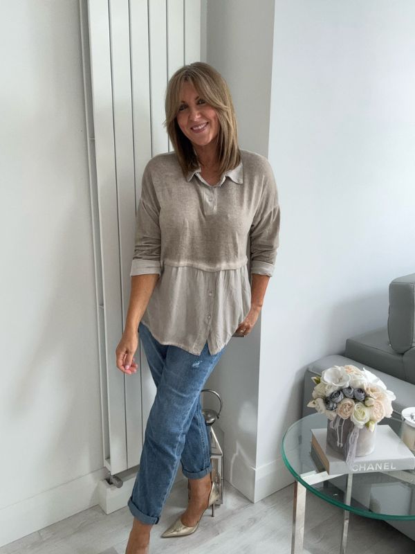 Woman wearing a vintage rose two-tone blouse with button details, paired with blue jeans and gold pointed flats, standing indoors by a round glass table and a flower arrangement.