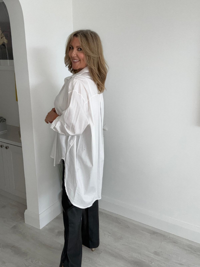 Model wearing an oversized white shirt with a detachable black tie, featuring a button-down front, long sleeves, and curved hem, styled for a modern, chic look.
