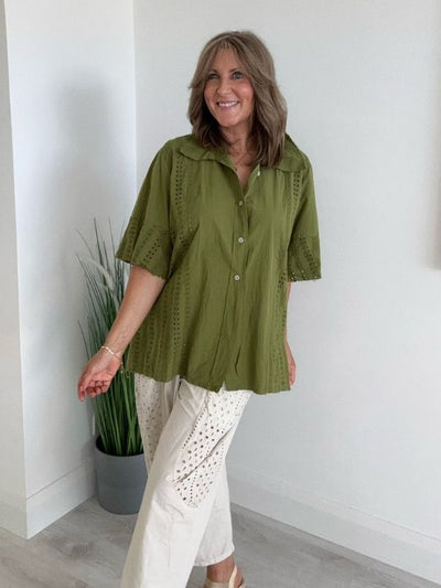 Woman wearing a relaxed green cotton button-up shirt with broderie detailing and wide-leg cream embroidered trousers