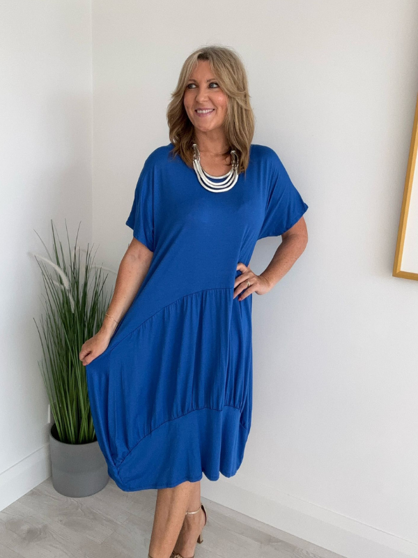 Model wearing a relaxed fit tunic dress with an asymmetric tiered hem, short sleeves, and round neckline, styled for casual comfort and everyday elegance