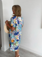 Woman wearing a colorful dress with abstract face designs against a white wall.