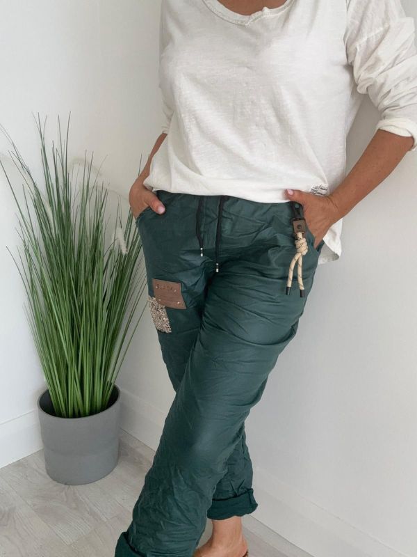 Women’s leatherette joggers in faux leather with soft fleece lining, elastic waistband, adjustable drawstring, side pockets, and patch detail. 