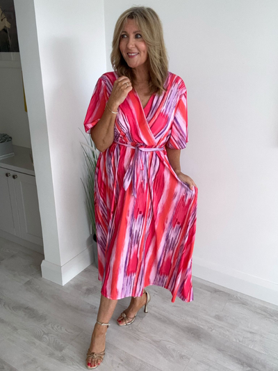 Model wearing a vibrant pink-red abstract wrap midi dress with short sleeves and tie waist, styled for summer elegance