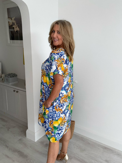 Model wearing a knee-length tunic dress with a bold Mediterranean lemon and scroll print, featuring a relaxed fit, short sleeves, and side pockets, styled for a fresh and breezy summer look