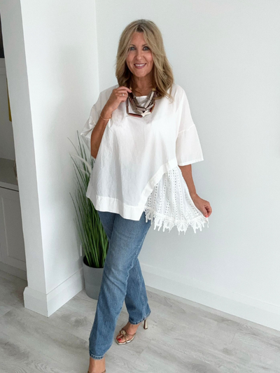 Woman wearing an asymmetric cotton top with lace side detail, styled with jeans and heels