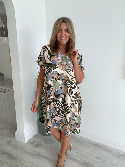 Model wearing a knee-length tunic dress with an all-over abstract floral print in green, peach, and blue tones, styled with strappy heels for a relaxed summer look