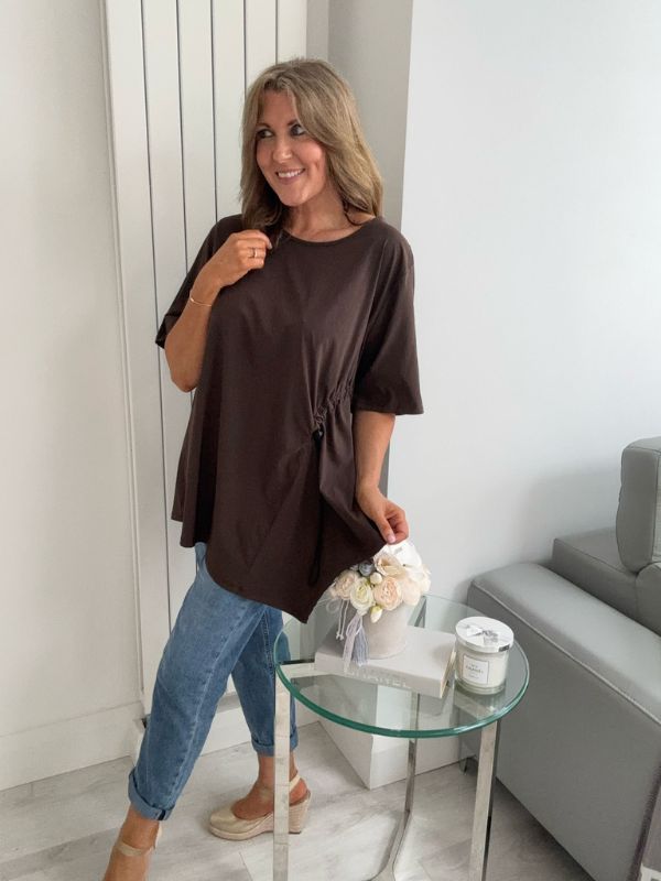 Woman wearing Dark Brown asymmetrical drawstring tunic top with jeans and statement necklace
