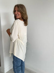 Woman wearing cream asymmetrical drawstring tunic top with jeans and statement necklace