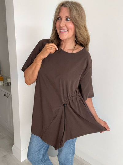Woman wearing Dark Brown asymmetrical drawstring tunic top with jeans and statement necklace