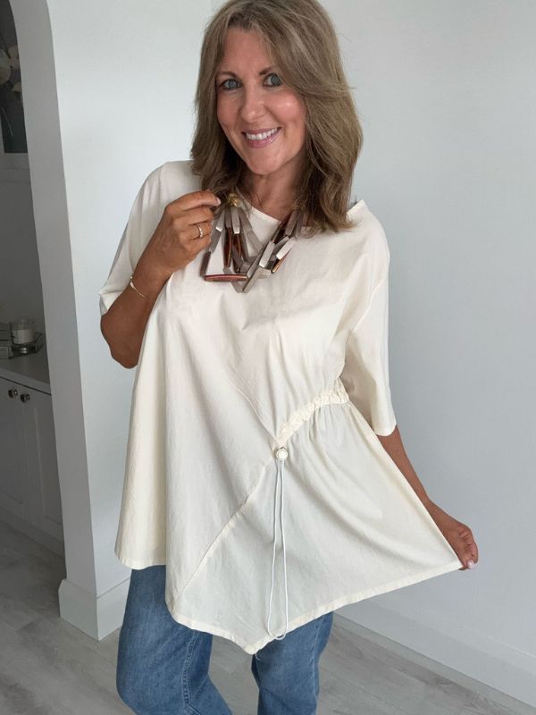 Woman wearing cream asymmetrical drawstring tunic top with jeans and statement necklace