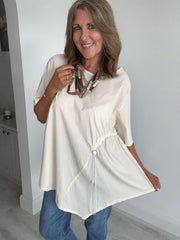 Woman wearing cream asymmetrical drawstring tunic top with jeans and statement necklace